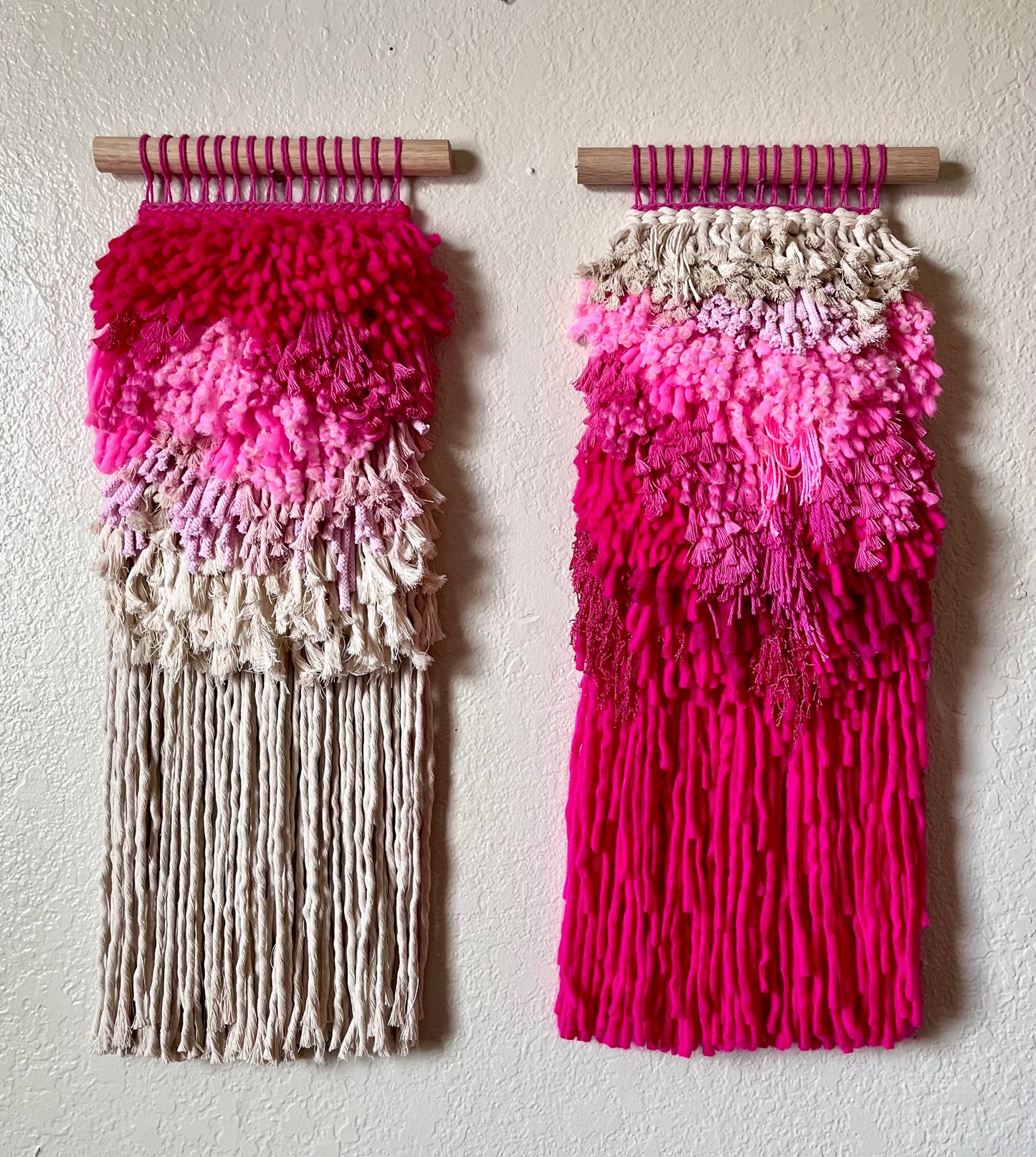 Two wall hangings with pink and white ombre design on a plain background
