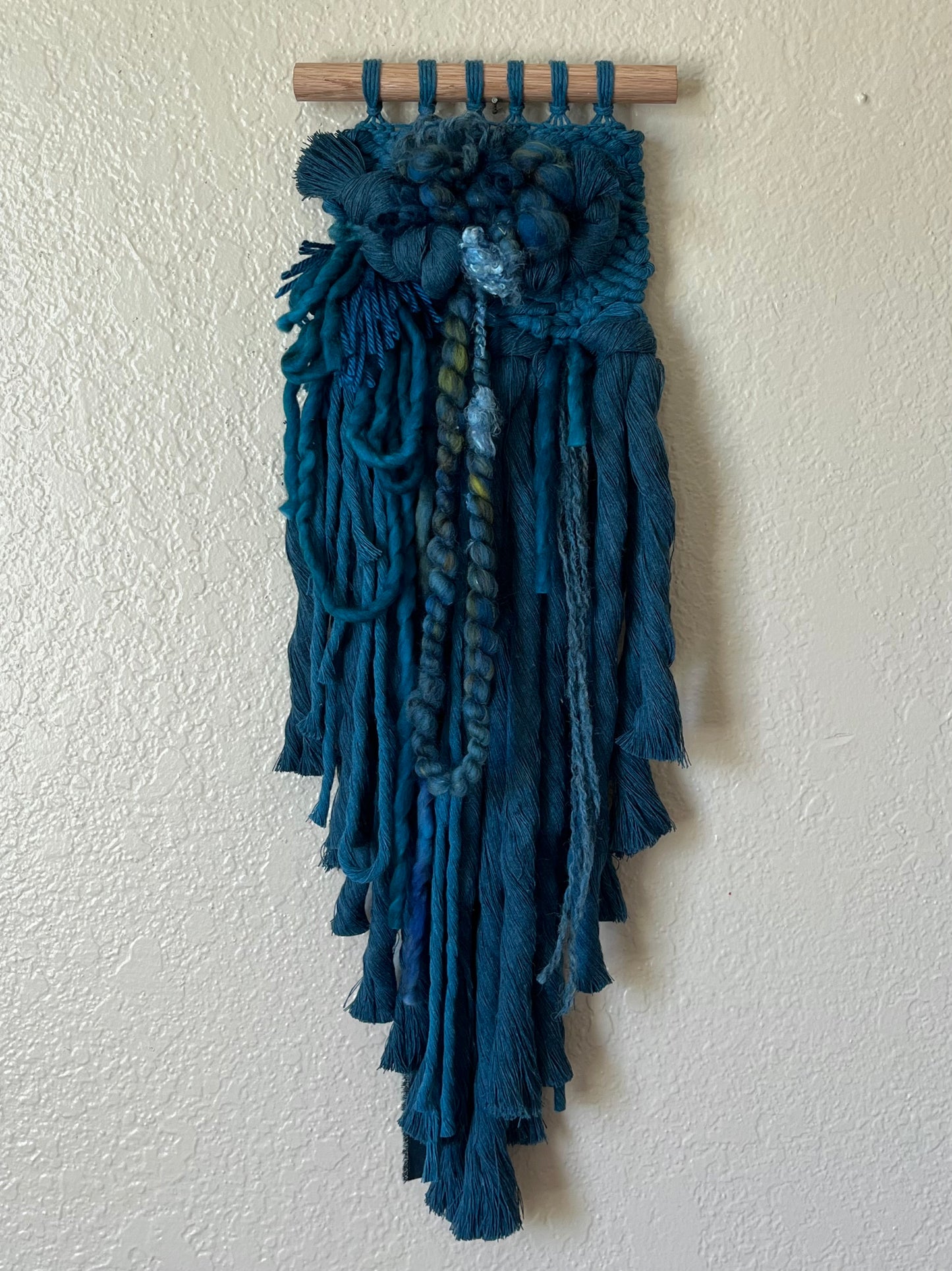 teal monochrome woven wall hanging on a wooden rod against a white wall