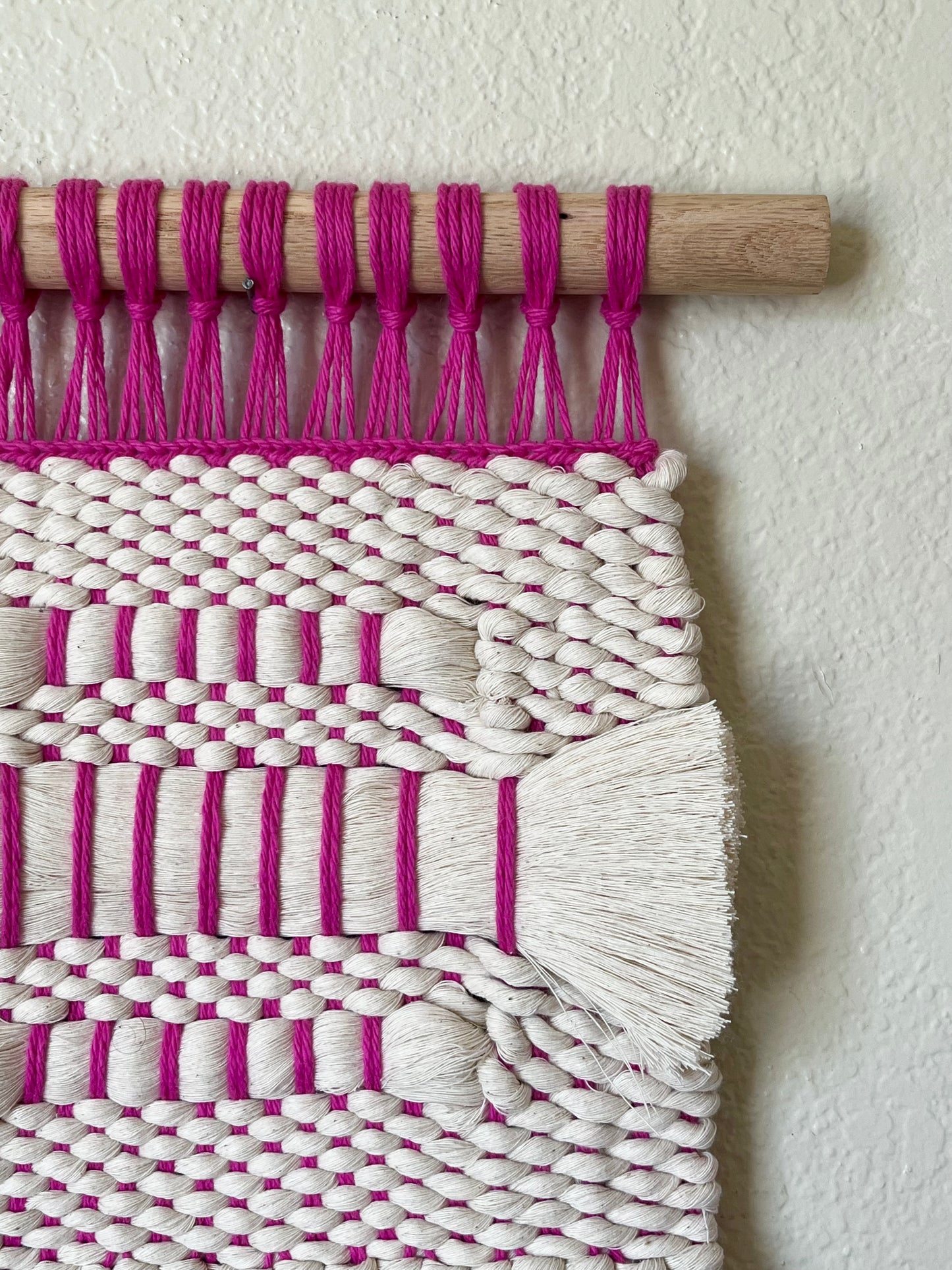 Woven wall art with pink and white pattern on a plain background