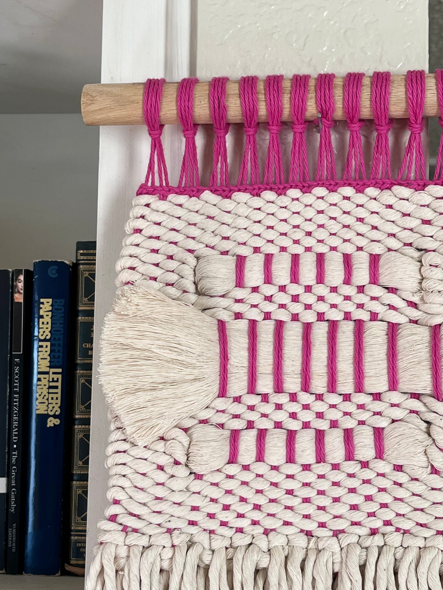 Woven wall art with pink and white pattern on a plain background