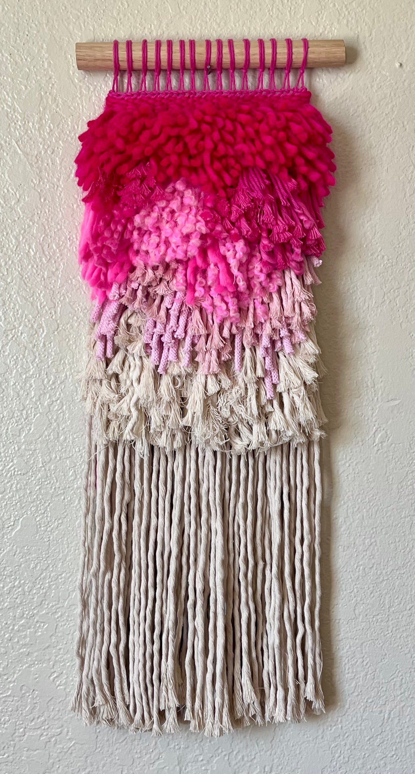 Woven wall art with pink to white gradient on a plain background